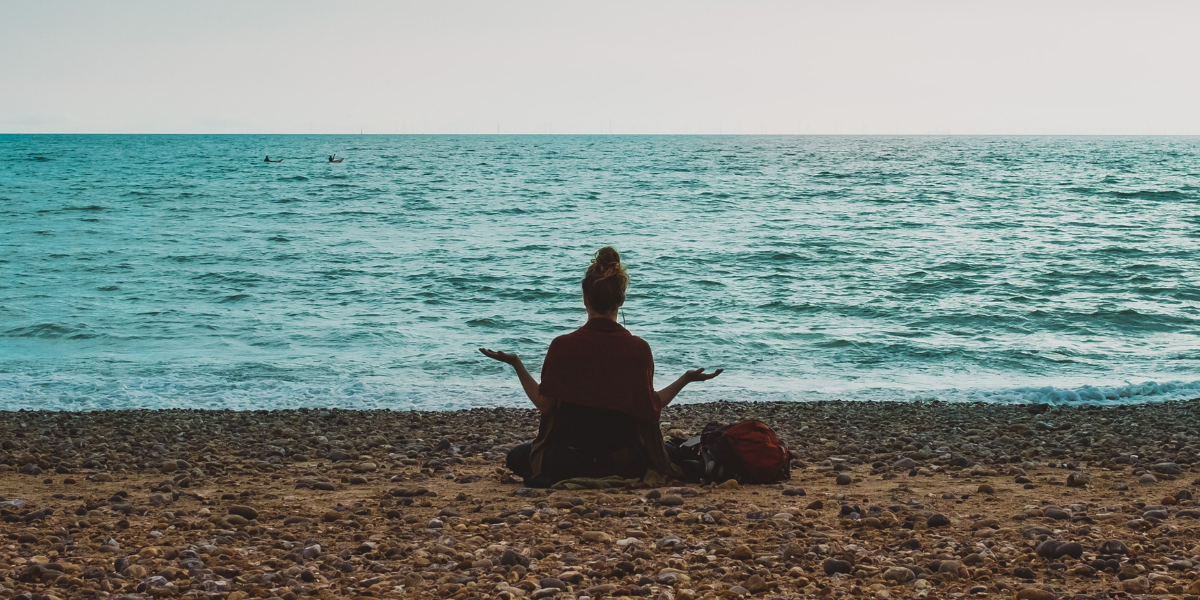 A woman meditates on a beach.
