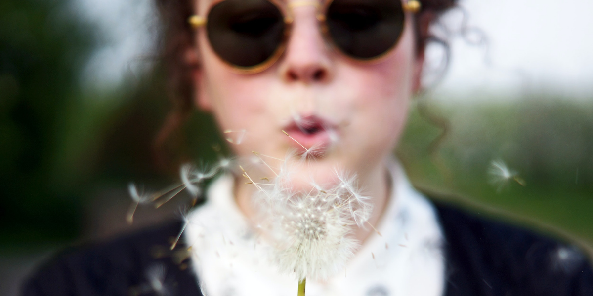 A woman blows the seeds from a dandelion, perhaps making a wish in the process.